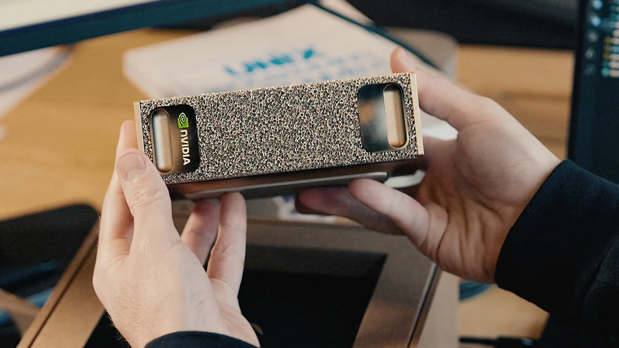 NVIDIA DGX Spark held in two hands over a desk, showing the champagne-gold metal-foam front face with the NVIDIA logo.